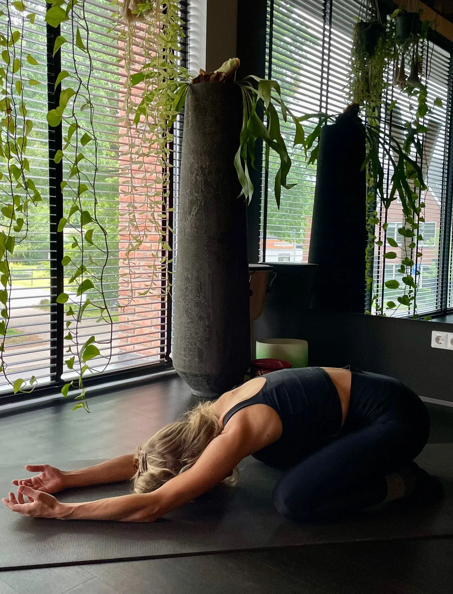Vrouw in de kindhouding op de mat, naast de planten bij het raam